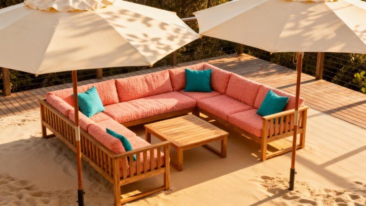 Teak sectional with coral and teal cushions under ivory umbrellas on sandy deck