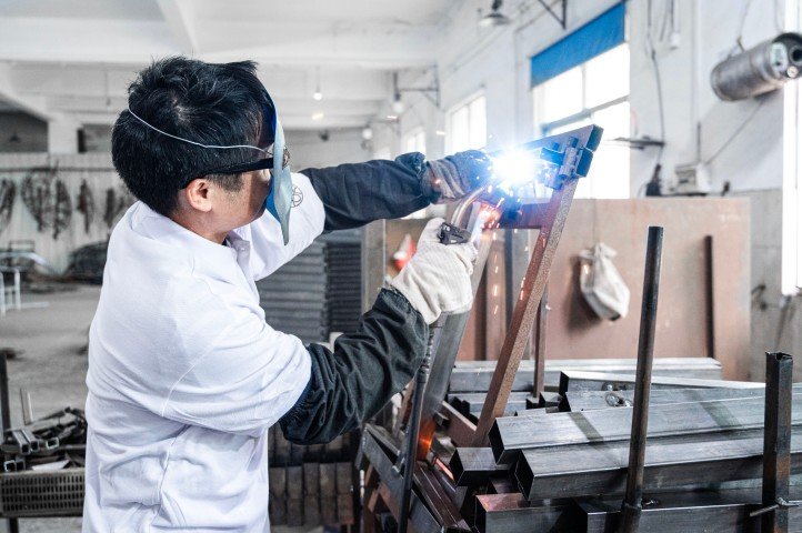 Welder assembling mild-steel patio chair frame styled as wrought iron