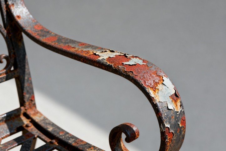 Inspecting rust and paint failure on wrought iron chair arm